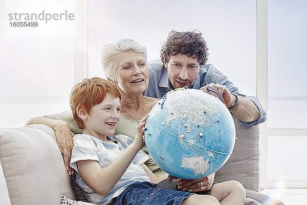 Großmutter  Vater und Enkel sitzen auf einer Couch in einer Villa und betrachten einen Globus