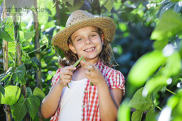 Lächelndes Mädchen pflückt Bohnen im Garten