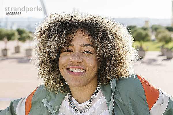 Glückliche junge Frau mit gelocktem Haar an einem sonnigen Tag