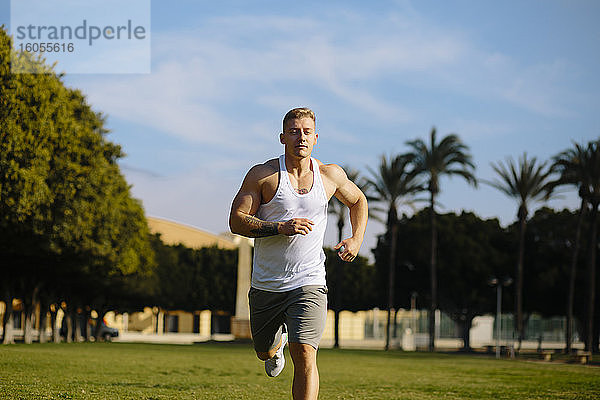 Männlicher Sportler  der an einem sonnigen Tag im Park gegen den Himmel läuft