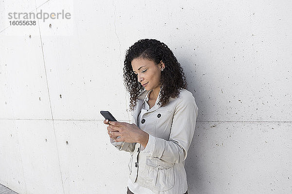 Stilvolle Geschäftsfrau  die ein Smartphone benutzt  während sie an der Wand steht