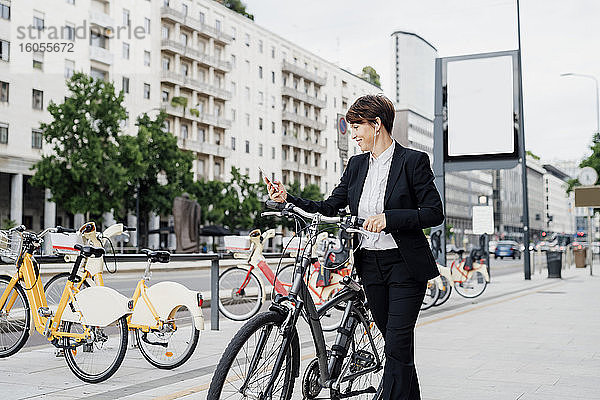 Geschäftsfrau hört Musik  während sie mit dem Fahrrad auf dem Gehweg in der Stadt spazieren geht