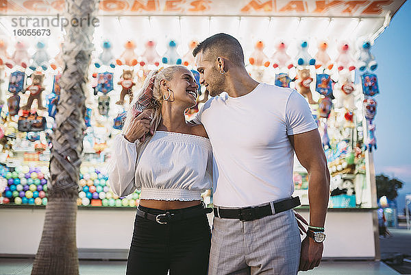 Romantischer Mann  der seine glückliche Freundin ansieht  während er in einem Vergnügungspark an einem Stand steht