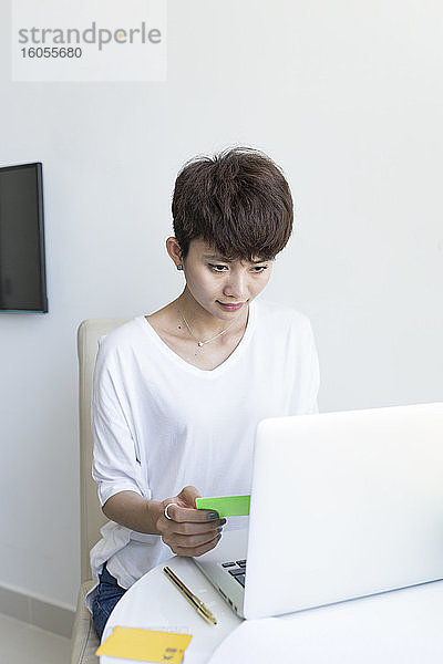 Junge Frau mit kurzen Haaren beim Online-Shopping am Laptop zu Hause