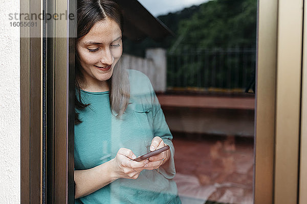 Frau mit Smartphone am Fenster  Mann mit Laptop zu Hause auf dem Bett liegend