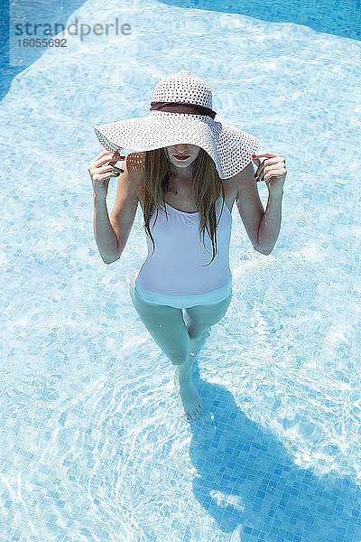Junge Frau mit Hut schwimmt an einem sonnigen Tag im Pool eines Ferienortes