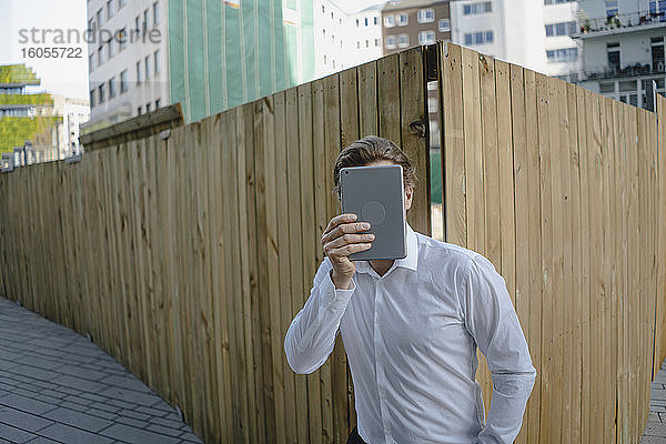 Geschäftsmann bei einem Boarding in der Stadt  der sein Gesicht mit einem Tablet bedeckt