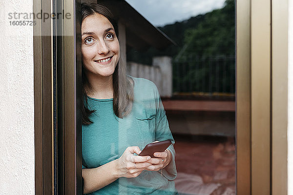 Frau mit Smartphone am Fenster  Mann mit Laptop zu Hause auf dem Bett liegend