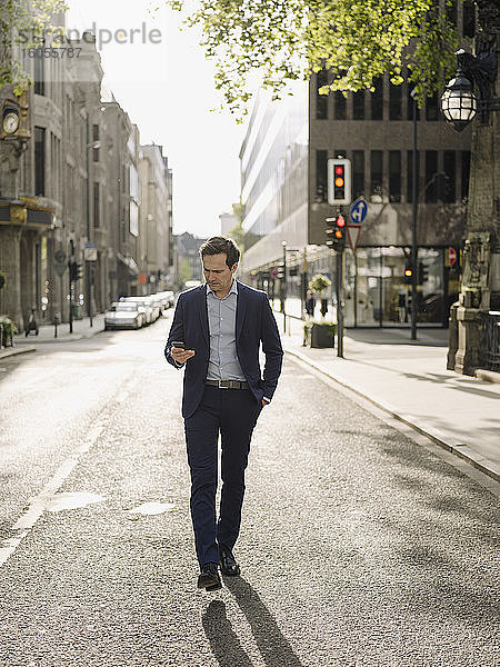 Älterer Geschäftsmann  der auf einer Straße in der Stadt spazieren geht und ein Smartphone benutzt
