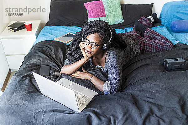 Junge Frau mit Laptop  die zu Hause auf dem Bett einen Film ansieht