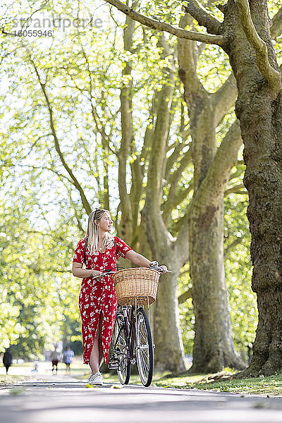 Frau schaut weg  während sie mit dem Fahrrad auf dem Gehweg in einem öffentlichen Park spazieren geht
