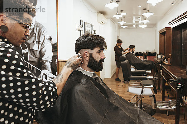 Trendiger Friseur  der die Haare eines Kunden im Salon stylt