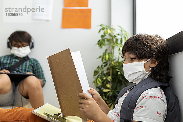 Jungen mit Masken  die in der Schule in einiger Entfernung sitzend lernen