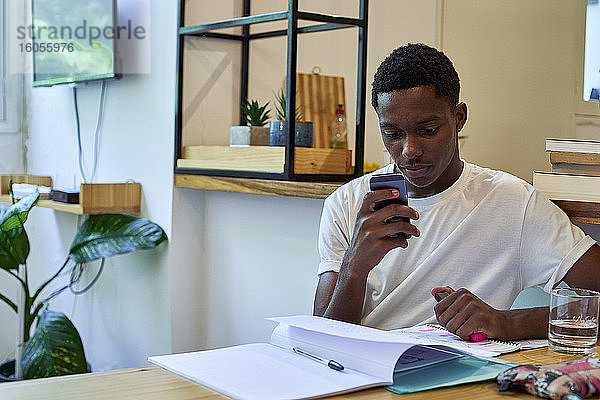 Junger Mann benutzt sein Smartphone beim Lernen auf dem Tisch zu Hause