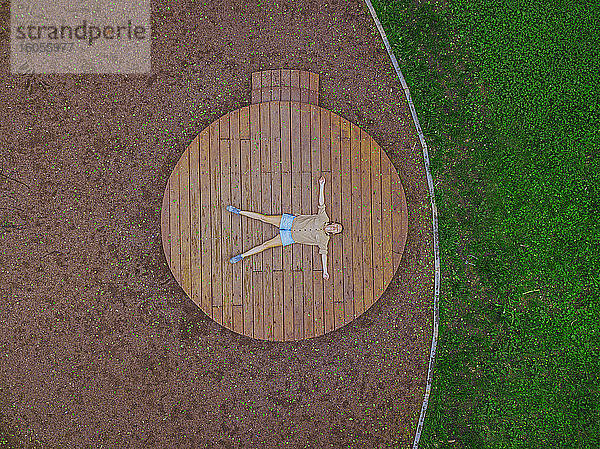 Drohnenaufnahme einer Frau  die auf einer Holzbühne im Park liegt