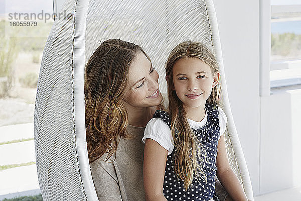 Porträt einer lächelnden Mutter und ihrer Tochter  die in einem Hängesessel sitzen