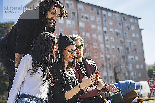 Freunde schauen auf das Smartphone einer jungen Frau in der Stadt