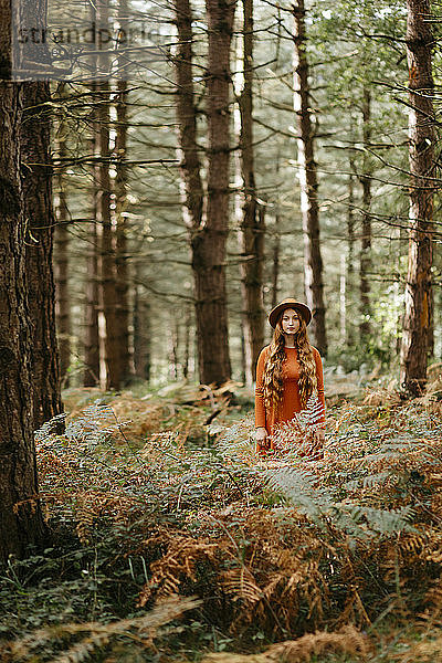 Junge Frau mit langen Haaren und Hut steht inmitten von Pflanzen im Wald
