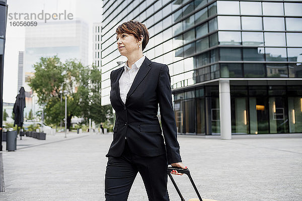 Weiblicher Unternehmer mit Koffer zu Fuß auf der Straße gegen moderne Gebäude in der Stadt