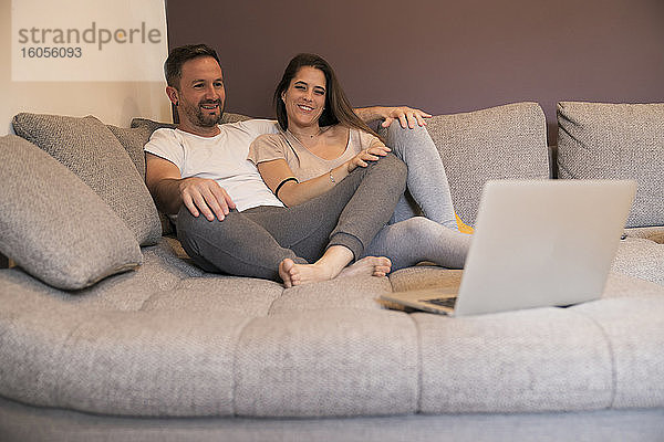 Paar sieht sich einen Film auf dem Laptop an und entspannt sich auf dem Sofa zu Hause