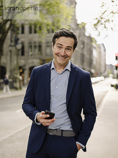 Porträt eines glücklichen reifen Geschäftsmannes mit Smartphone in der Stadt