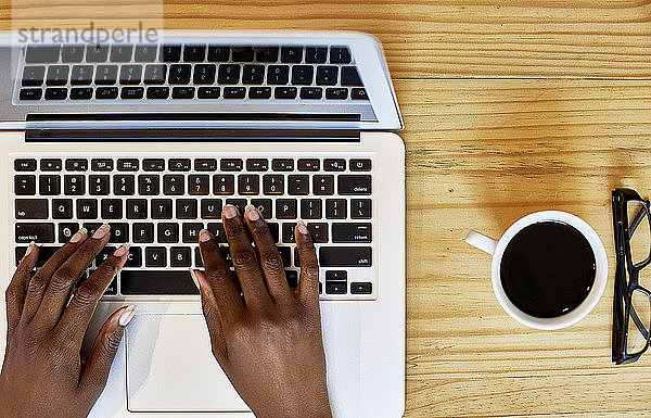 Abgeschnittene Hände einer Frau  die einen Laptop auf einem Holztisch zu Hause benutzt
