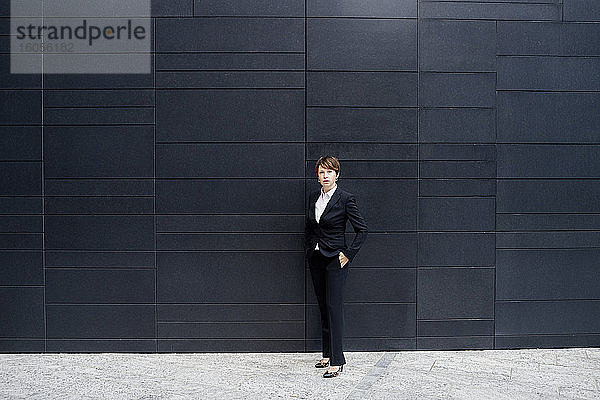 Selbstbewusste Geschäftsfrau steht auf dem Bürgersteig vor einem modernen Gebäude in der Stadt