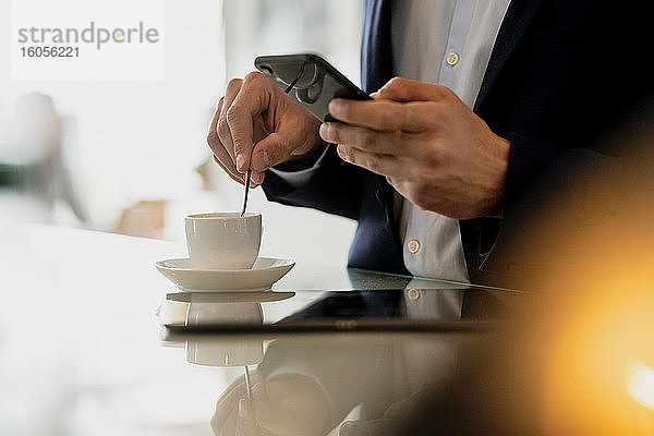 Nahaufnahme eines männlichen Berufstätigen  der sein Smartphone benutzt  während er Kaffee auf dem Tresen eines Cafés mischt