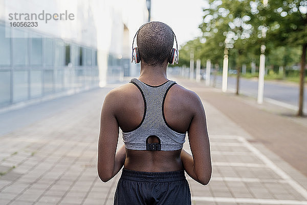 Junge Frau mit rasiertem Kopf hört Musik über Kopfhörer  während sie auf einem Fußweg steht