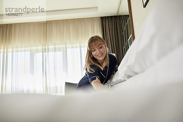 Lächelndes Zimmermädchen  das im Hotelzimmer stehend das Bett macht