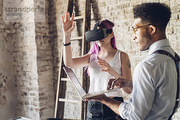 Zwei kreative Geschäftsleute mit VR-Brille und Laptop im Loft-Büro