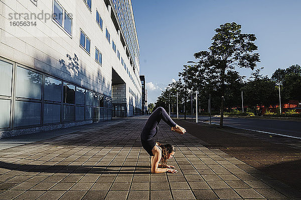 Junge Frau beim Yoga auf dem Bürgersteig in der Stadt an einem sonnigen Tag