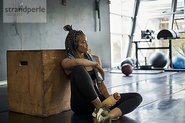 Nachdenkliche Sportlerin hört Musik  während sie im Fitnessstudio auf dem Boden sitzt