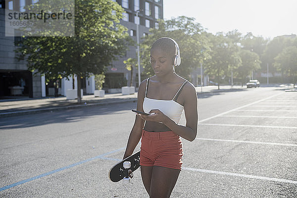 Junge Frau hört Musik über Kopfhörer und benutzt ein Mobiltelefon  während sie auf der Straße geht