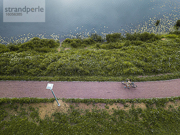 Russland  Tichwin  Luftaufnahme einer Radfahrerin  die auf einem Fußweg am Seeufer im Park eine Pause einlegt