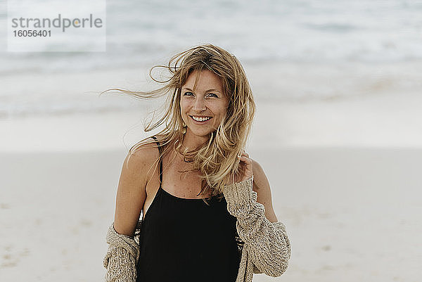 Porträt einer lächelnden erwachsenen Frau mit blondem Haar  die am Meer steht