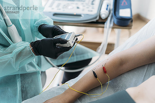 Arzt in Schutzkleidung untersucht den Arm einer Frau mit Elektroden