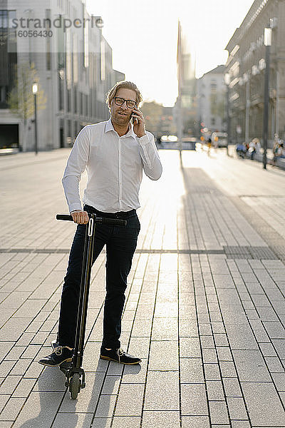 Geschäftsmann mit Kick-Scooter am Telefon in der Stadt