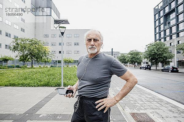 Selbstbewusster älterer Mann hört Musik  während er auf einem Fußweg in der Stadt steht