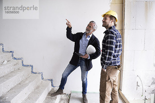 Männlicher Architekt  der einen Bauarbeiter anleitet  während er auf einer Treppe bei der Renovierung eines Hauses steht