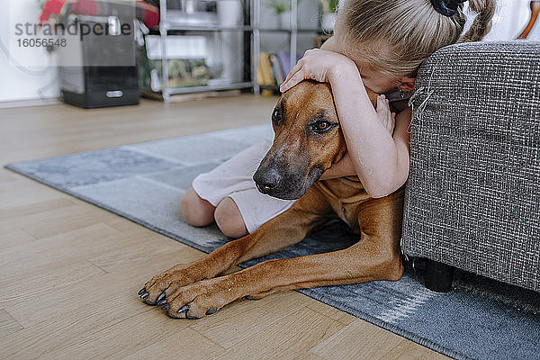 Mädchen umarmt Hund beim Entspannen auf Teppich im Wohnzimmer zu Hause