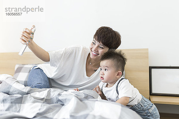 Lächelnde Mutter nimmt Selfie mit niedlichen Sohn auf Bett zu Hause