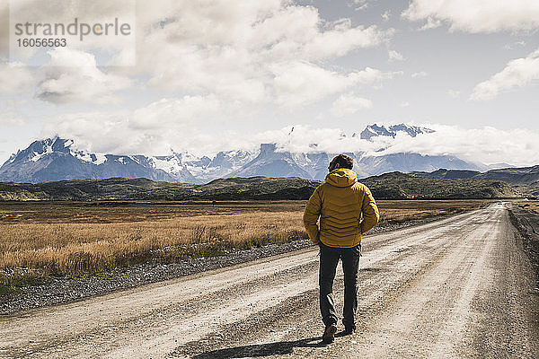 Älterer Mann  der auf einer unbefestigten Straße gegen den bewölkten Himmel läuft  Torres Del Paine National Park  Patagonien  Chile