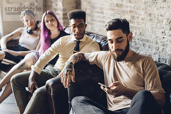Gruppe von Freunden sitzt mit Smartphone auf dem Sofa in einem Loft