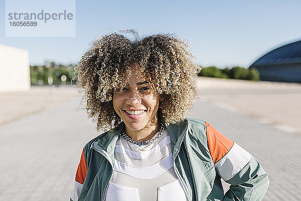 Selbstbewusste junge Frau mit lockigem Haar an einem sonnigen Tag