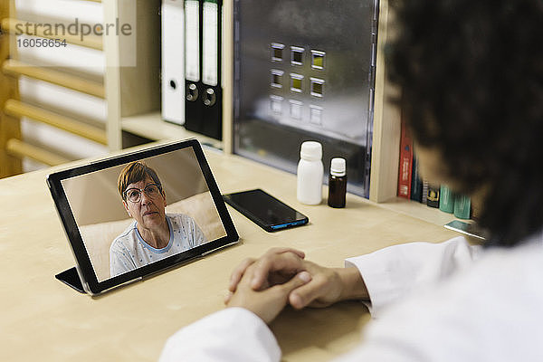 Ältere Frau auf digitalem Tablet-Bildschirm während Videogespräch mit Arzt