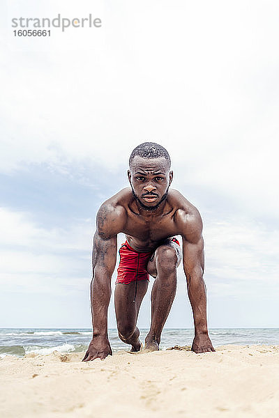 Sportlicher Mann in Startposition am Strand
