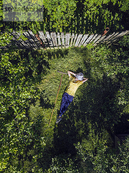 Luftaufnahme einer mittleren erwachsenen Frau mit den Händen hinter dem Kopf  die auf einer Wiese im Garten ruht