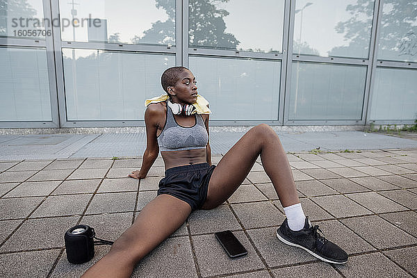 Müde Sportlerin mit rasiertem Kopf auf dem Fußweg in der Stadt sitzend
