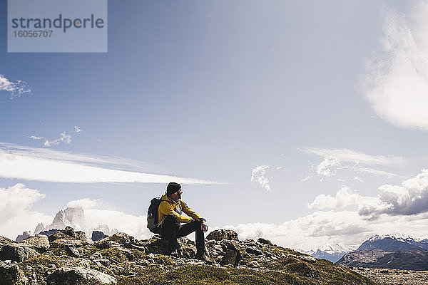 Männlicher Wanderer auf einem Berg sitzend gegen den Himmel an einem sonnigen Tag  Patagonien  Argentinien